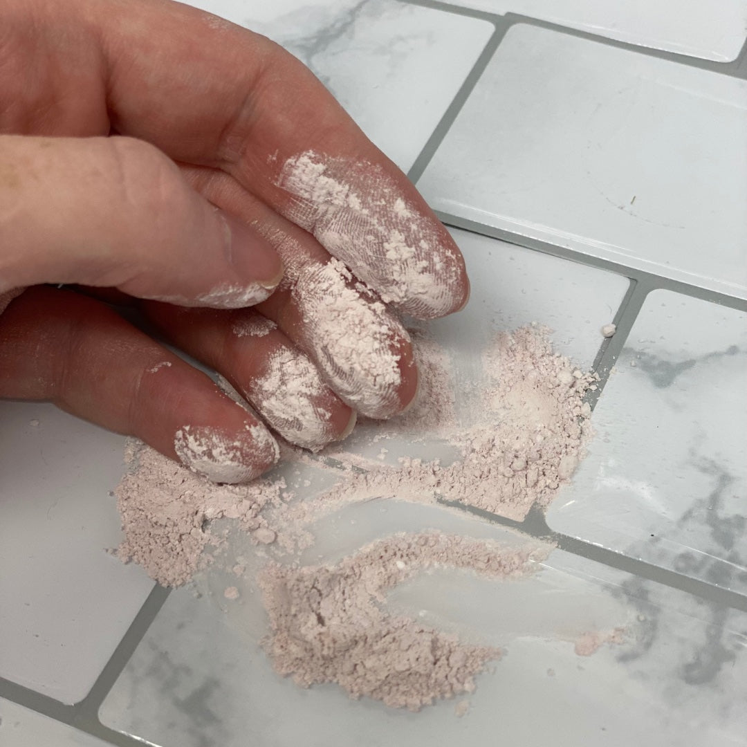 Aussie Pink Clay Cleanser Powder on bathroom floor with hand. 